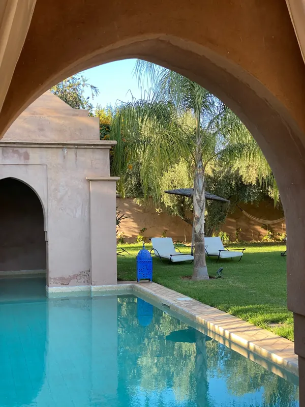 Piscine vue sous une arche, palmier et transats sur la pelouse
